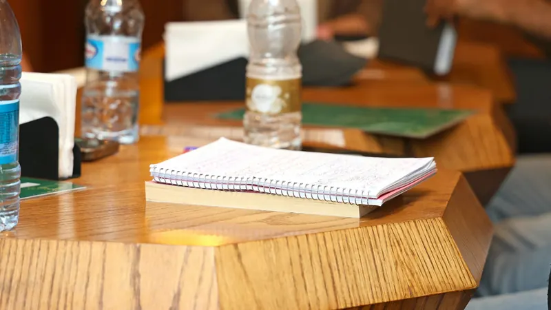 A spiral notebook and water bottles on a wooden meeting table